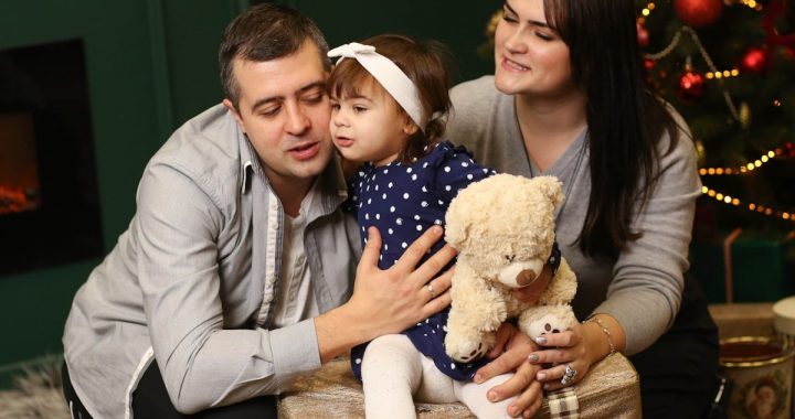 a man, woman and child sitting in front of a christmas tree
